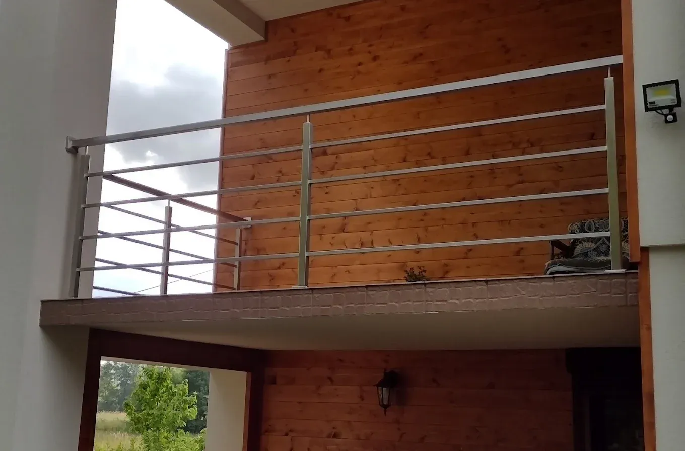 Balustrada balkonowa z nierdzewnych profili przy drewnianej elewacji